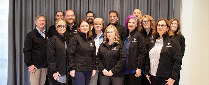 A group of insurance agents are standing together with matching black jackets with a North American Insurance Services logo smiling at the camera
